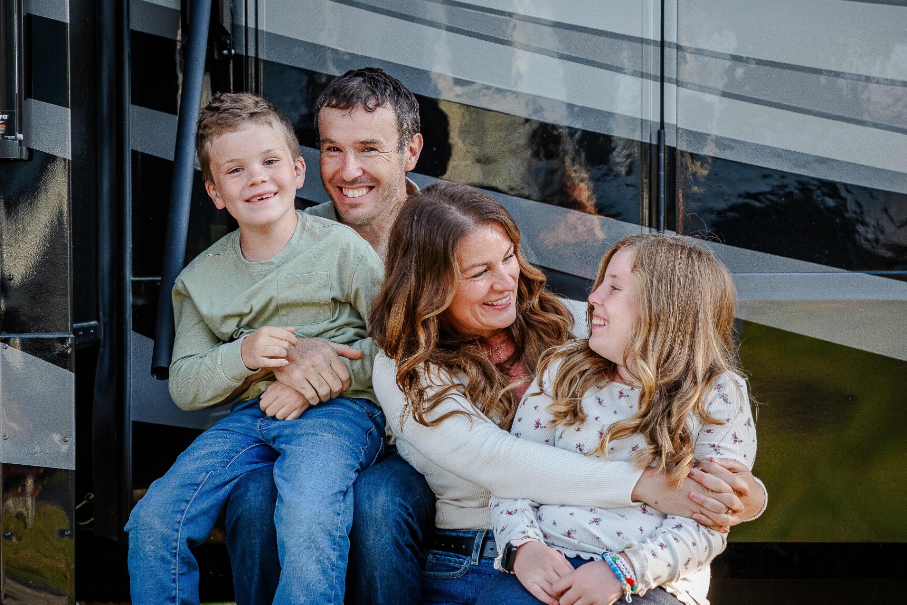 The Moss family — Nathan, Marissa, Hensley, and JJ — laughing together on the steps of their RV